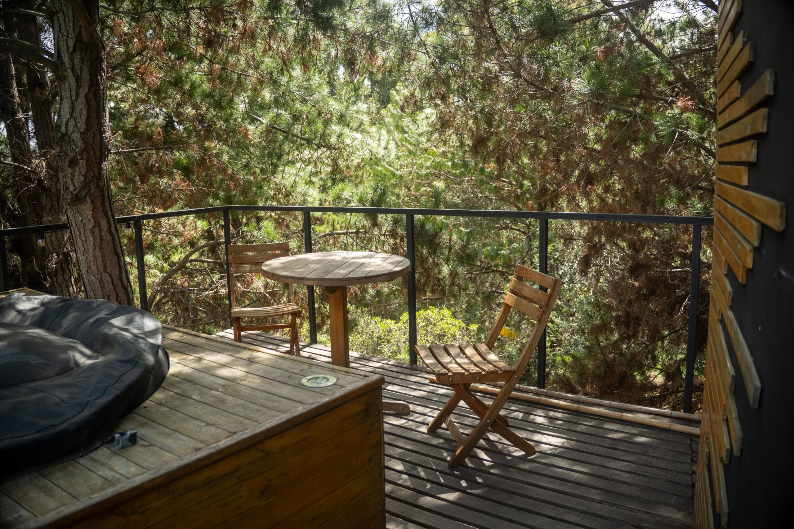 Services Peaceful outdoor balcony surrounded by trees with wooden chairs and table, perfect for relaxation.