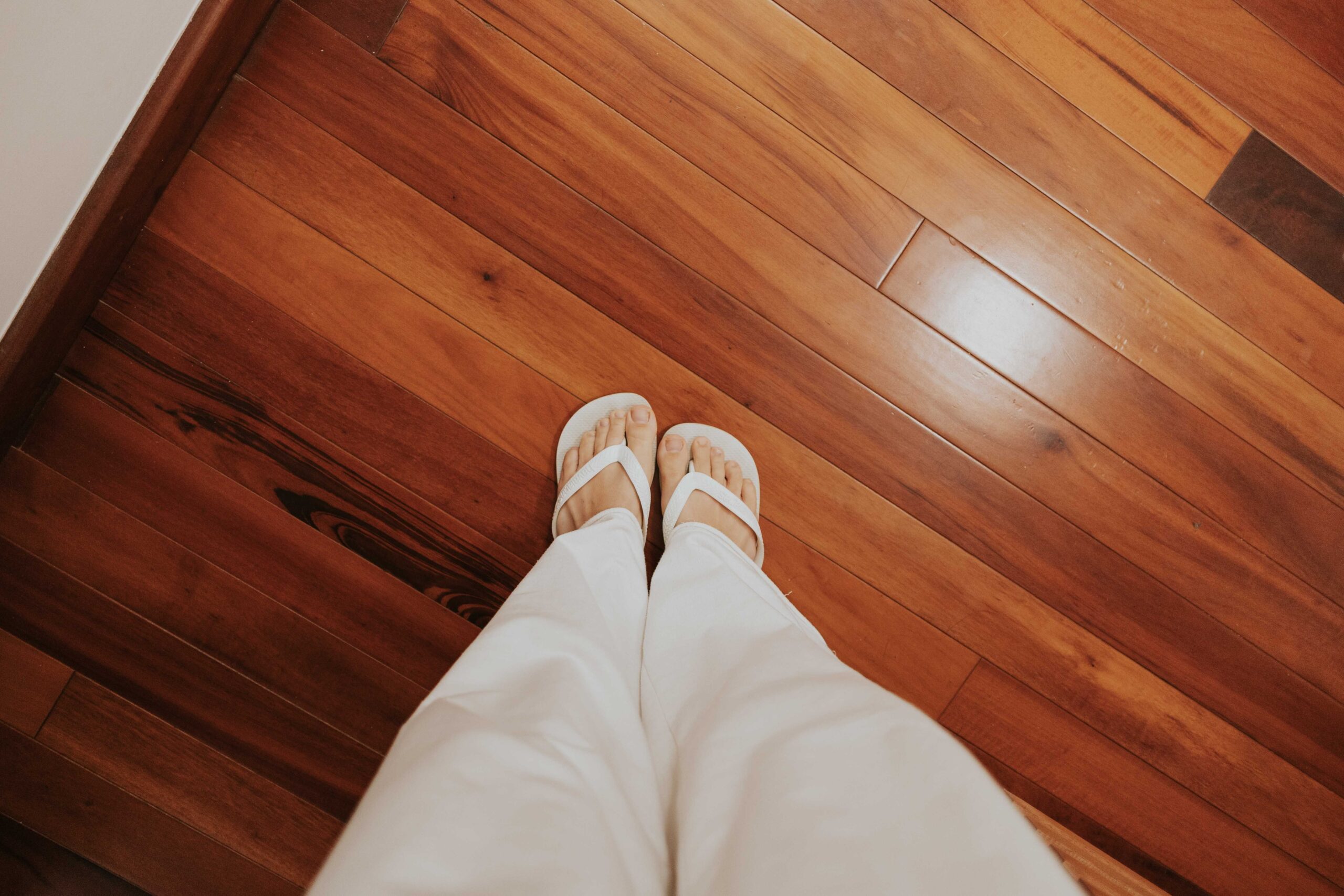 Services View of person wearing flip-flops and white pants standing on a wooden floor.