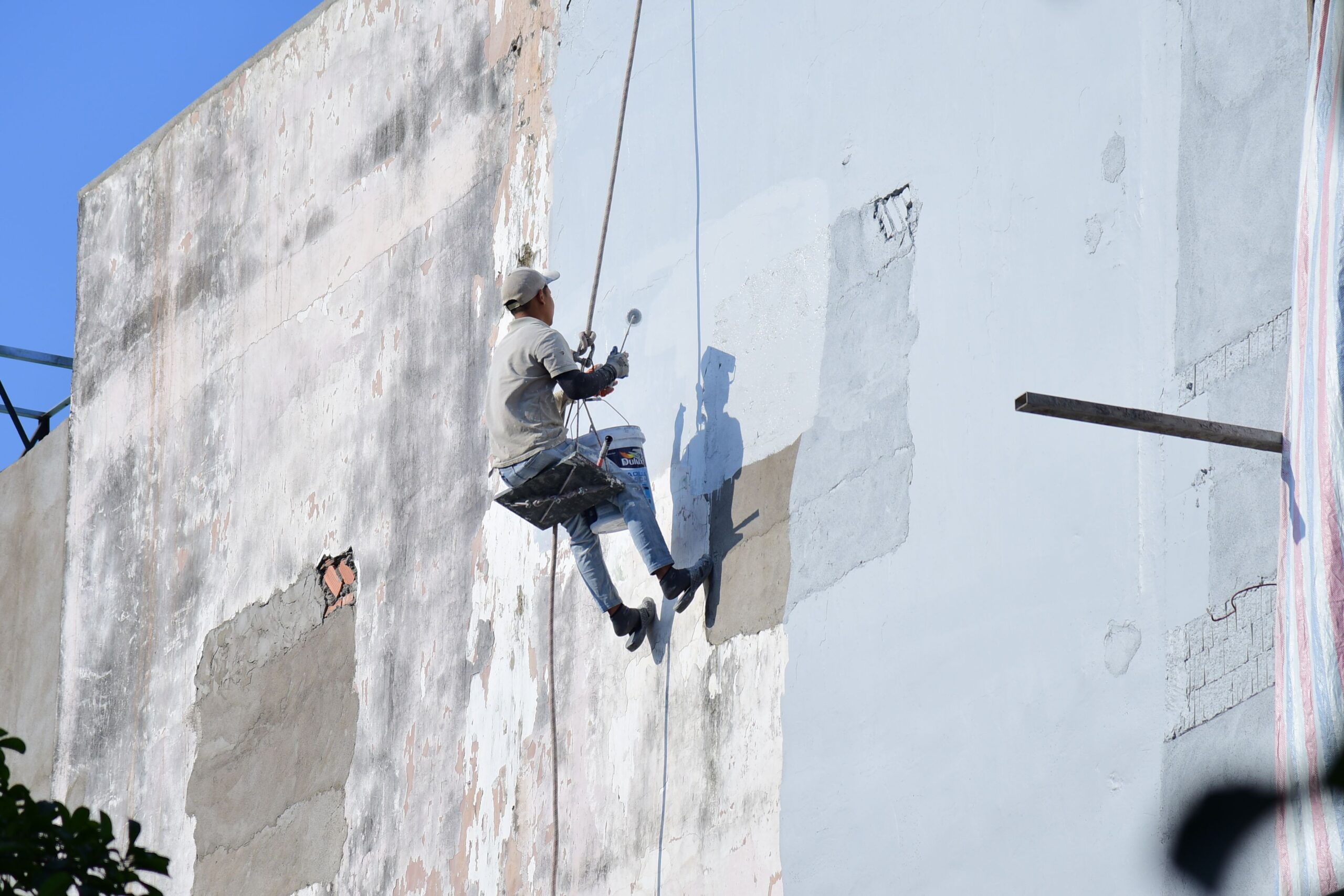 Services A rope access worker suspended while painting a high-rise building facade.